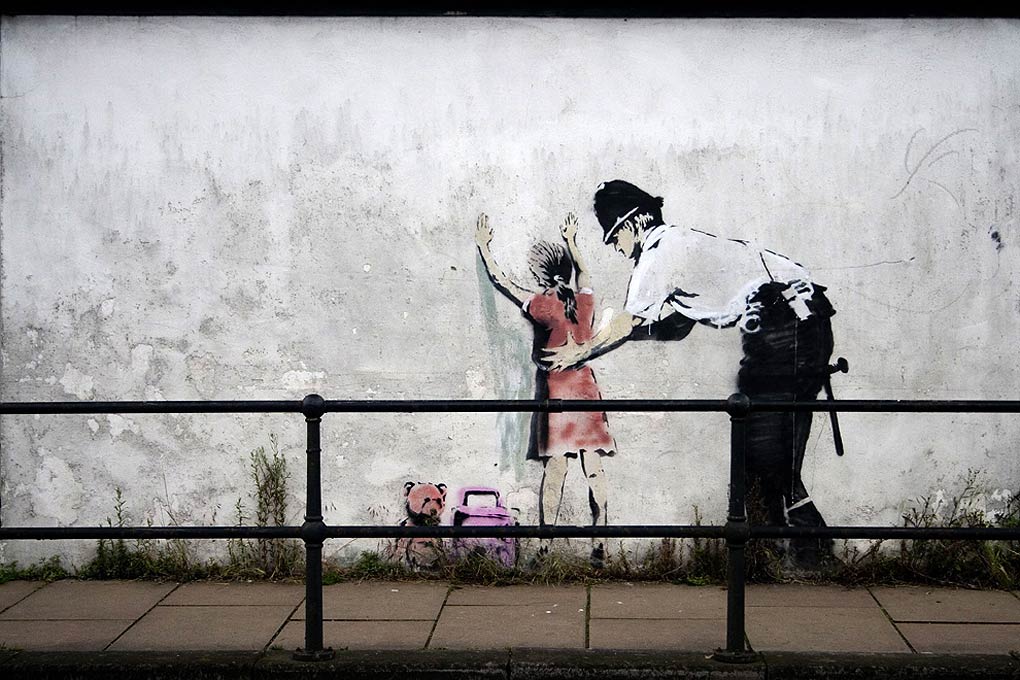 Graffiti de Banksy : policier fouillant une enfant contre un mur