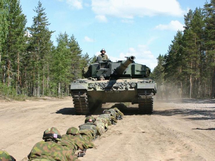 Char militaire avançant vers caméra, soldats allongés en avant-plan, paysage désertique