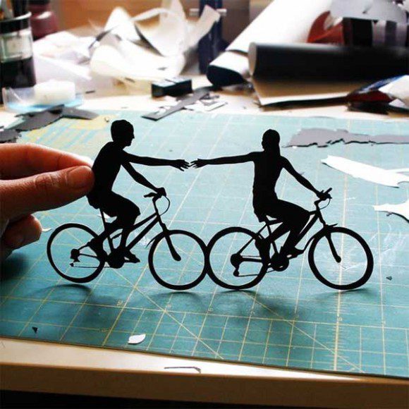 Art papier découpé montrant deux silhouettes à vélo se tenant la main sur grille
