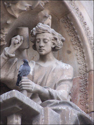 Sculpture en pierre d'une femme classique tenant un oiseau bleu sur son épaule.