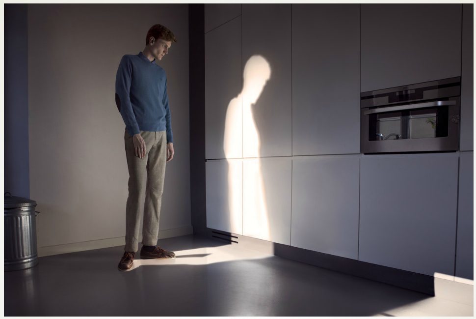 Jeune homme face à l'ombre d'une silhouette projetée sur mur blanc moderne