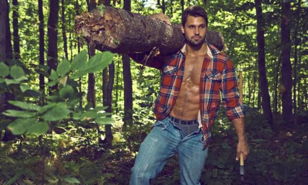 Homme torse nu en chemise à carreaux dans une forêt, tenant un rocher