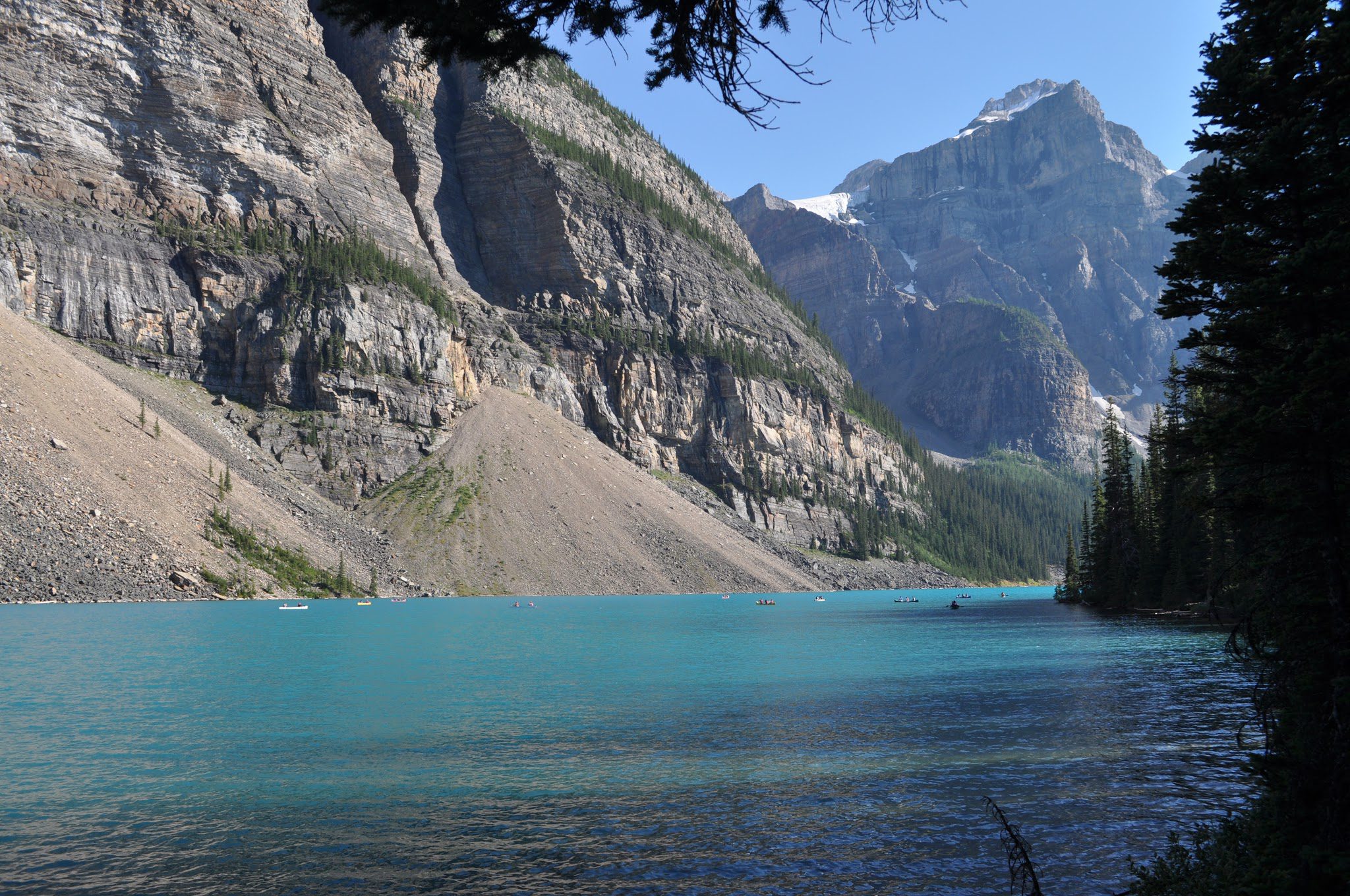 Vallée alpine avec lac turquoise, dense forêt de conifères et montagne enneigée