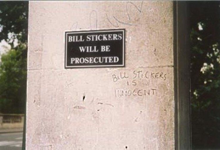 Mur de pierre avec panneau « Bill Stickers Will Be Prosecuted » et graffiti « Bill Stickers Is Innocent »