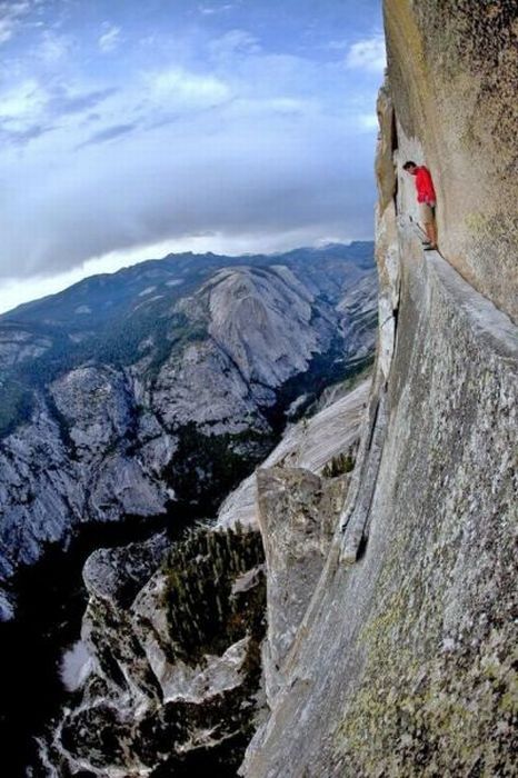 Grimpeur en tee-shirt rouge escaladant paroi rocheuse vertigineuse, montagnes alpines en arrière-plan