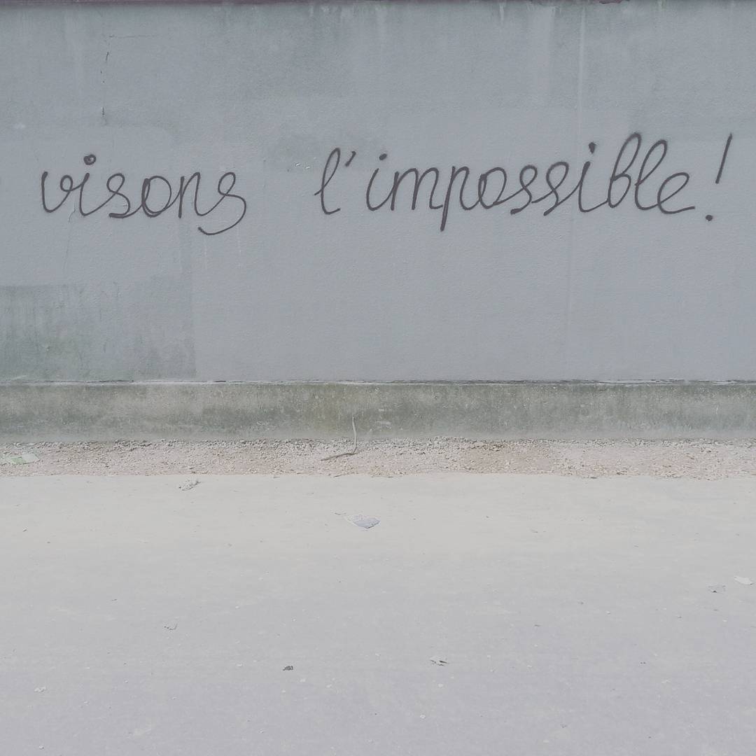 Texte manuscrit « Visons l'impossible ! » gravé sur un mur gris