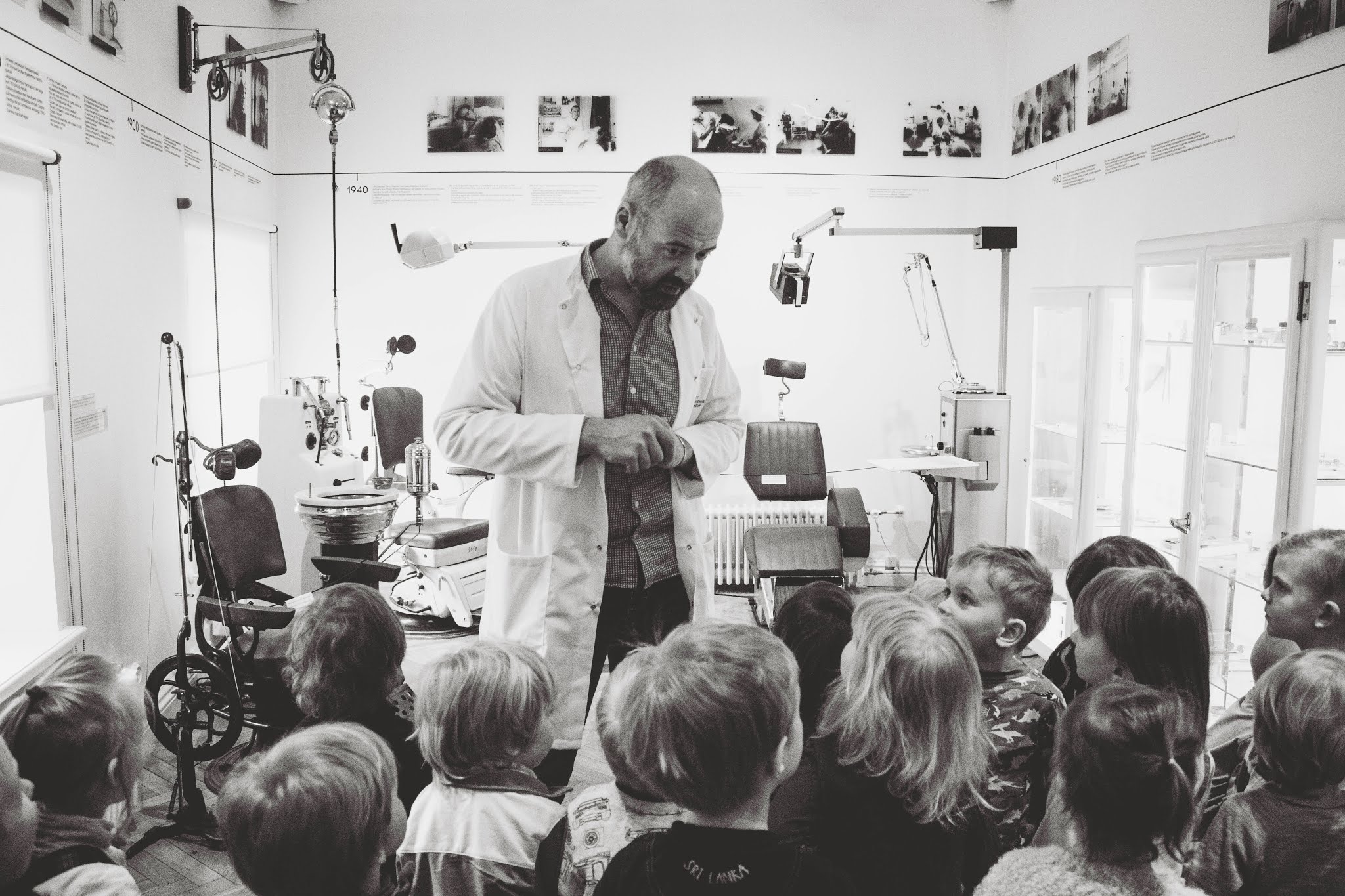 Photo historique noir et blanc - homme en blouse blanche montrant un instrument scientifique à des enfants dans un laboratoire