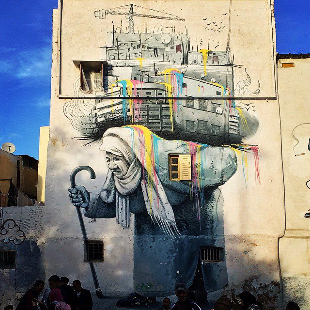 Fresque murale street art : femme voilée tenant un balai avec des couleurs arc-en-ciel émanant de sa tête