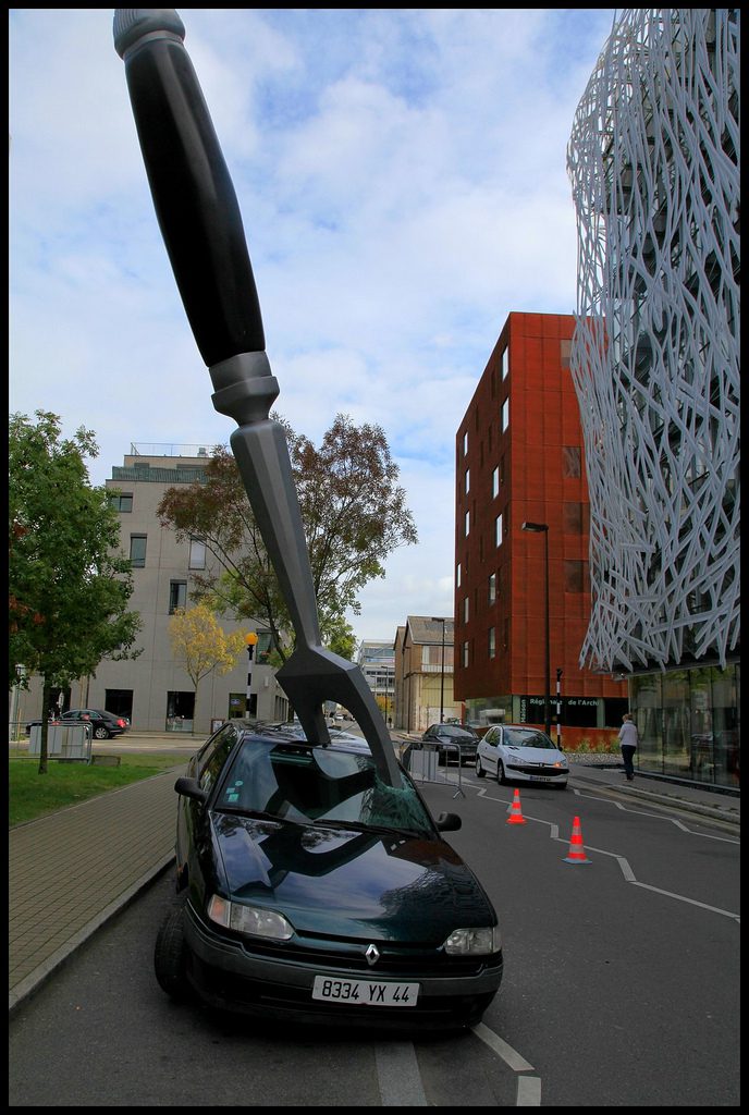 Sculpture urbaine : main géante noire transpercant une automobile en milieu urbain