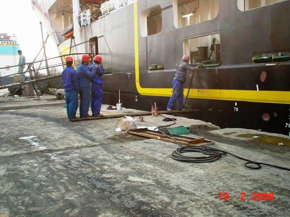 Ouvriers en combinaison bleue et casques rouges travaillant à la base d'un navire