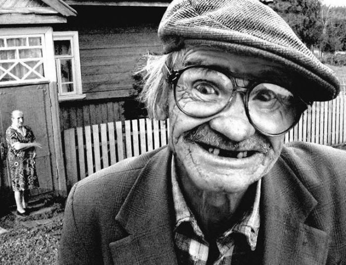Photo en noir et blanc d'un homme âgé souriant avec casquette et lunettes rondes