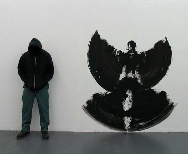 Personne vêtue de noir de dos devant dessin abstrait noir et blanc sur mur gris
