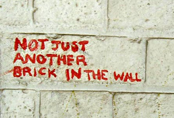 Graffiti en lettres rouges sur mur de briques blanches : « Not just another brick in the wall »